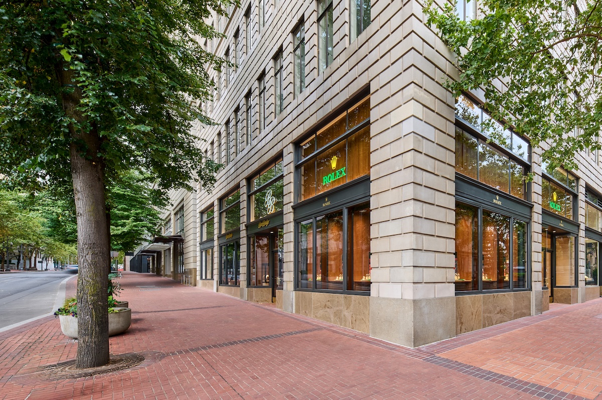 A street corner view of the Ben Bridge Rolex showroom in downtown Portland on a tree-lined street with red brick sidewalks. 